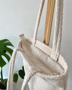 a white purse hanging from a hook on a wall next to a potted plant