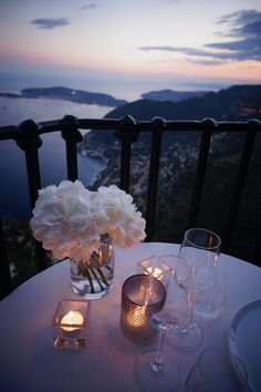 the table is set with wine glasses, candles and white flowers in glass vases