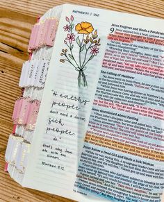 an open bible on a wooden table with flowers and words written in the book pages