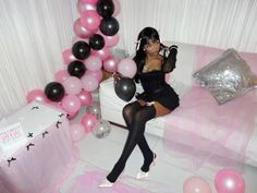 a woman sitting on top of a bed next to pink and black balloons