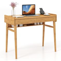 a laptop computer sitting on top of a wooden desk next to a vase with flowers