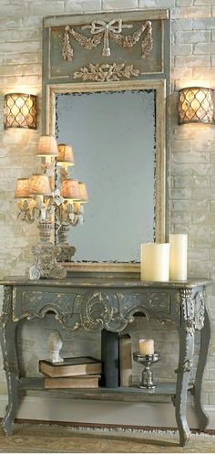 a mirror and some candles on a table in front of a brick wall with a chandelier