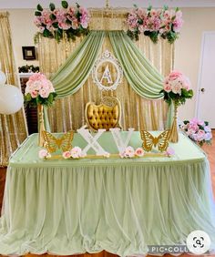 a green table topped with a gold chair next to a flower covered wall and white balloons