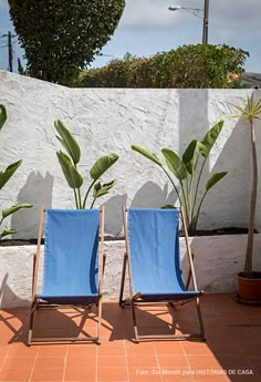 two blue lawn chairs sitting next to each other on a tiled floor in front of a white wall