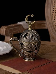 an ornate teapot on a table next to a white plate and wooden chair in the background