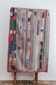 a multicolored patchwork quilt hanging on a wooden stand in front of a white wall