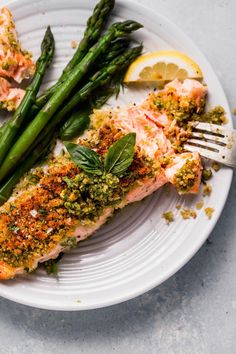 a white plate topped with fish and asparagus next to lemon wedges on a table