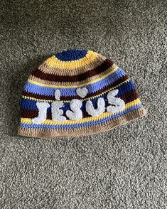 a crocheted hat with the word jesus written in white letters on it sitting on carpet