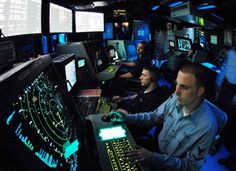 a man sitting in front of a computer monitor on top of a desk next to other people