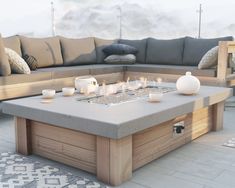 a fire pit sitting on top of a wooden table next to a gray couch and pillows