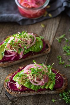 two slices of bread topped with veggies and sprouts on top of a wooden table