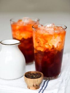 two glasses filled with ice and tea on top of a white towel next to a pitcher