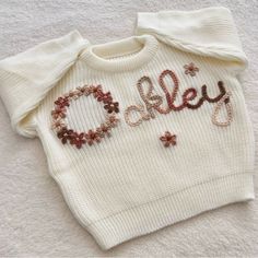 a white sweater with the word olley written in red and brown beads on it