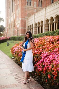 a woman in a white dress standing next to some pink and purple flowers with a blue sash