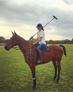 a woman riding on the back of a brown horse holding a mallet in her hand