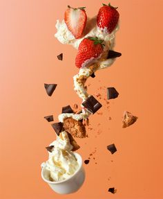 strawberries falling into a bowl of ice cream with chocolate chips on an orange background