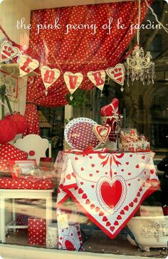 a window display with red and white hearts on it's windowsill, in front of a storefront