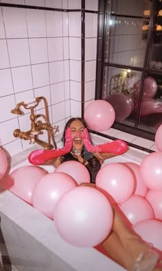 a woman laying in a bathtub surrounded by pink balloons