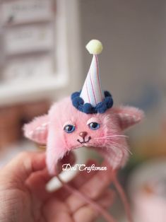 a tiny pink cat with a hat on it's head is being held by someone