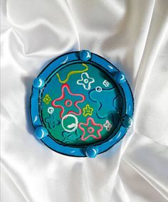 a blue plate with colorful designs on it sitting on a white cloth covered tablecloth