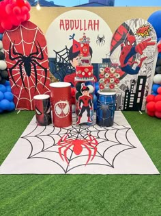 a spiderman themed birthday party with balloons and decorations on the grass in front of a backdrop