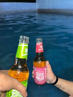 two people holding up beer bottles in front of a swimming pool