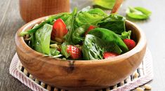 a wooden bowl filled with spinach and strawberries