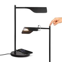 a person is pointing at a phone on a desk lamp