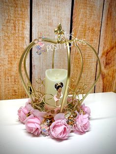 a white candle with pink flowers and gold trim around it on top of a table