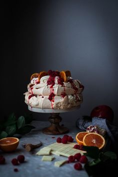 a cake with white frosting and fruit on the top is surrounded by oranges, raspberries, and other fruits