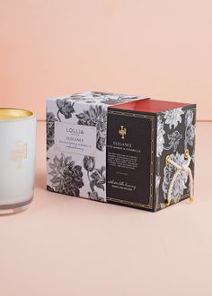 a candle next to a box on a pink surface with an image of a flower