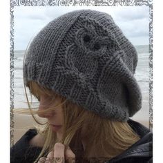 a woman standing on the beach wearing a knitted hat