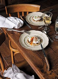 two plates with food on them sitting on a wooden table next to wine glasses and napkins