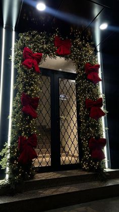 a door decorated with red bows and greenery in front of a building at night