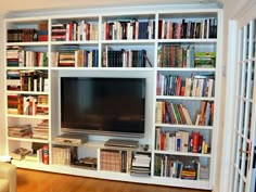 a living room filled with lots of books and a flat screen tv sitting on top of a white book shelf