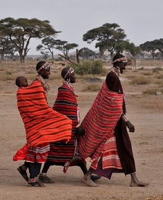 three women in colorful clothing walking across a dirt field