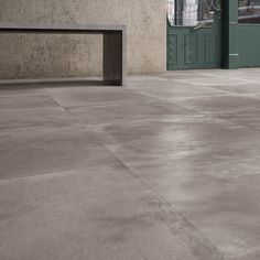 an empty concrete floor in front of a building with a green door and window on the side