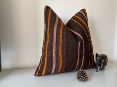 a brown and orange striped pillow sitting on top of a table next to a pine cone