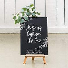 a chalkboard sign that says help us capture the love with greenery on it