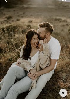 a man and woman are sitting on the ground together, smiling at each other as they hold their hands up