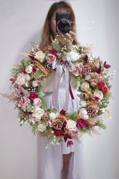 a woman taking a selfie in front of a wreath with flowers and leaves on it