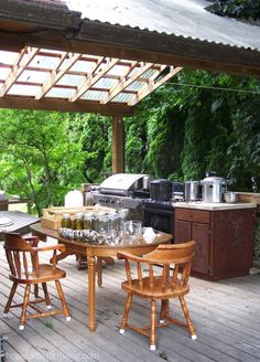 an outdoor kitchen and dining area on a deck with wood flooring, covered by a pergolated roof