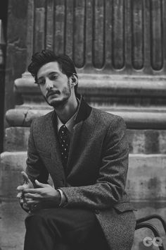 a man in a suit and tie sitting on a bench with his hands folded out