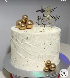 a white and gold birthday cake on a silver platter with two golden balls around it