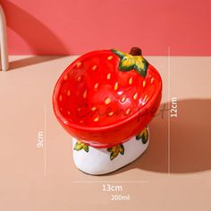 a strawberry shaped bowl sitting on top of a table next to a white chair and pink wall