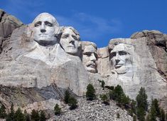 some very big statues that are on the side of a mountain with trees in front of them