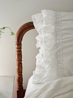 a bed with white ruffled pillows and a wooden headboard next to a plant