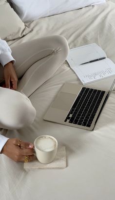 a woman sitting on a bed with her laptop and coffee