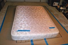 an unmade mattress sitting on top of a piece of cardboard with blue tape around it