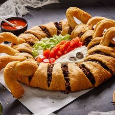 an elaborately shaped sandwich with meat and vegetables on it's side, surrounded by dipping sauces